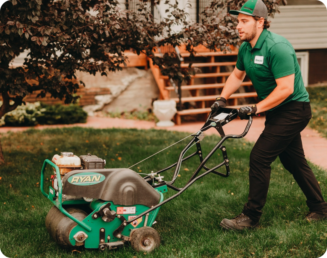 Yard Dawgs technician pushes an aerator over the lawn of a client